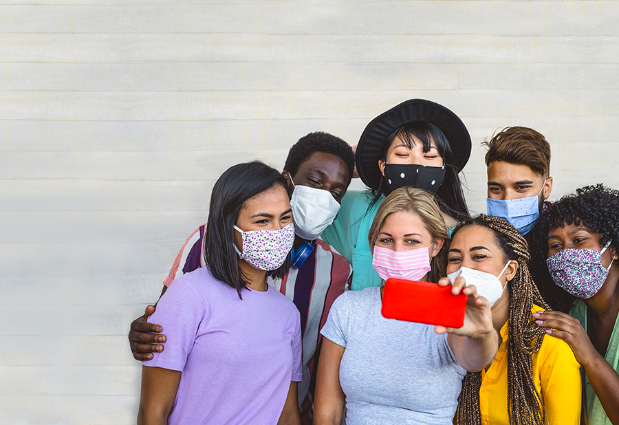 A group of young people, all wearing face masks, are taking a selfie together.